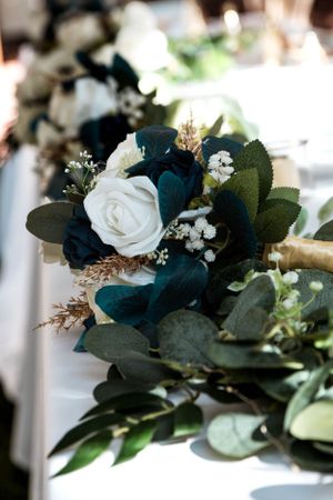 Elegant wedding bouquet featuring white roses, teal accents, and eucalyptus leaves arranged with baby's breath.