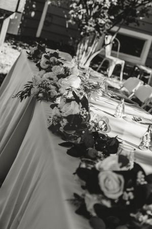 Black and white photograph of floral centerpieces and table settings at an elegant wedding reception.