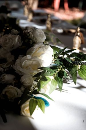Elegant white roses and greenery centerpiece arrangement on white tablecloth with soft lighting and bokeh effect.