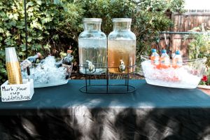 Glass beverage dispensers with ice buckets set up on a black tablecloth for an outdoor party or event service.