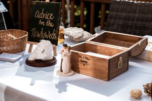 Rustic wooden box and chalkboard sign for wedding advice cards displayed on white tablecloth at outdoor reception.