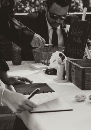 A black and white photograph showing people signing documents at a table with a small wedding cake topper.