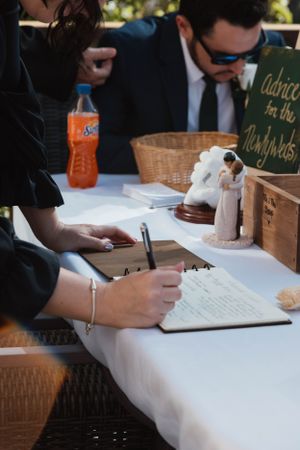 Someone signing a guestbook at a wedding reception with decorative details and orange soda on the table.