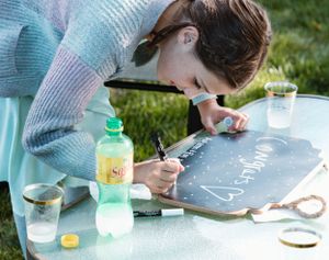 Someone writing on a chalkboard surface while crafting with mint and pastel colored supplies.