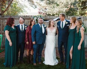 Wedding party in emerald green dresses and navy suits posing together in an outdoor garden setting.
