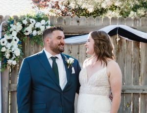 A couple shares a joyful moment under a floral arch at their outdoor wedding ceremony.