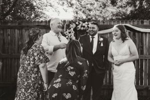 A candid outdoor wedding scene with guests gathered around in a backyard setting with a wooden fence.
