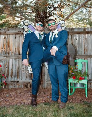 Two people in matching navy blue suits pose together in a backyard garden setting.