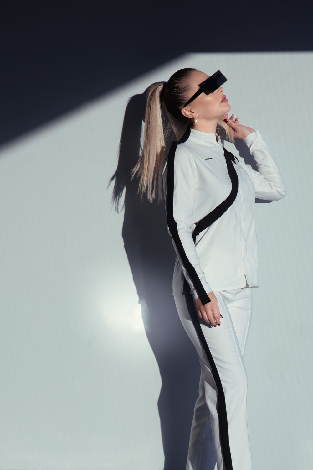 Model in a modest white suit, posing in a Genk parking lot with bright light and shadows with contrast.