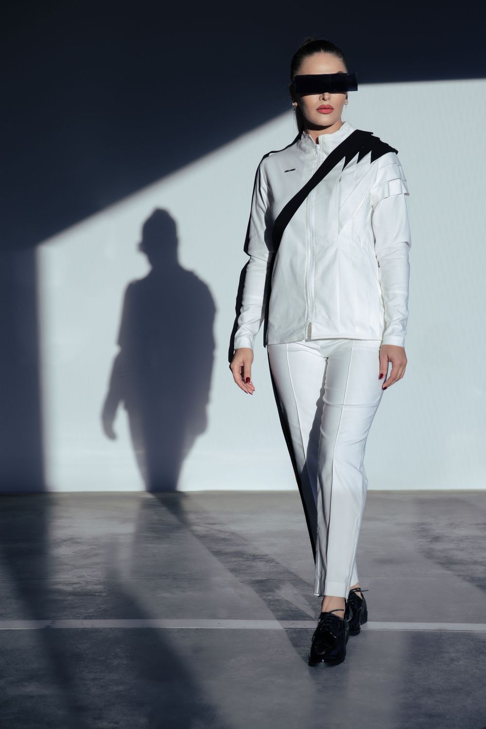 Model in a modest high-fashion suit, posing in a futuristic Genk parking lot with her silhouette shadow.