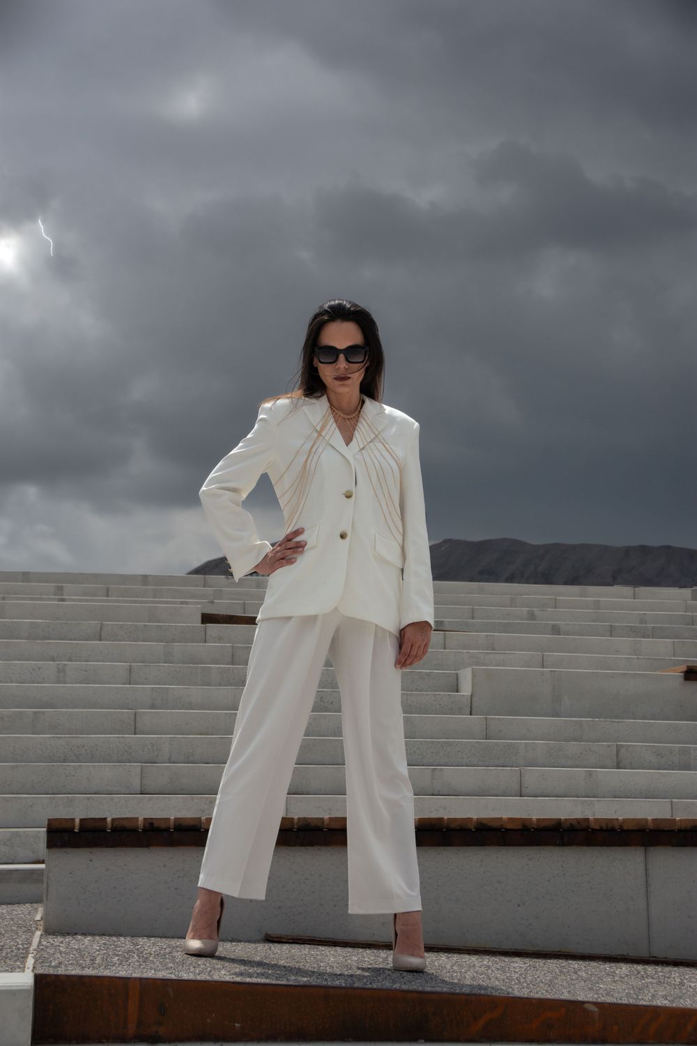 Model in sunglasses and a white modest suit, striking a fierce pose on the city stairs in Hasselt.