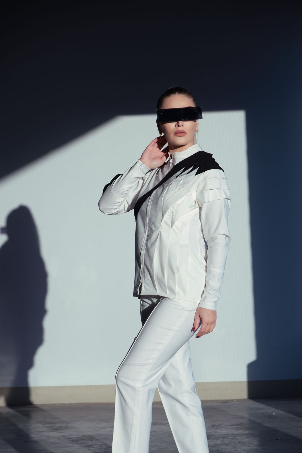 Model in a modest high-fashion suit with sunglasses, poses in a parking lot in Genk with a cool atmosphere.