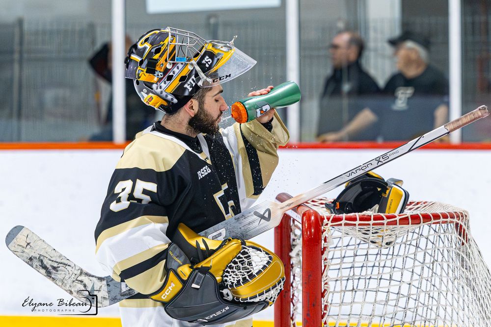 A hockey goalie makes a diving save attempt while defending the net during an intense game.