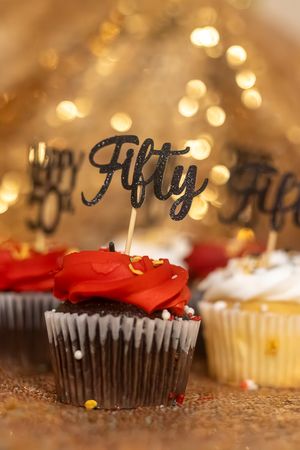 Chocolate cupcake with red frosting and a black glitter Fifty topper, surrounded by bokeh lights for a 50th birthday.