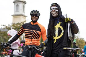 Two cyclists in athletic gear pose together with one wearing orange and the other in black with reflective accessories.