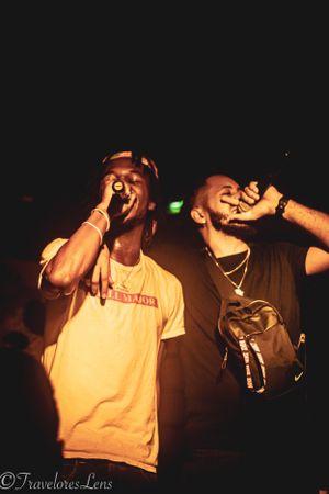 Two performers energetically singing into microphones on a dark stage.