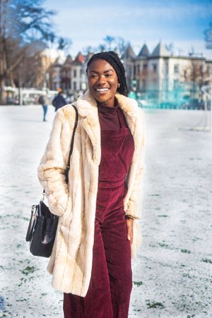 Person in burgundy outfit and cream fur coat smiling on a snowy winter day.