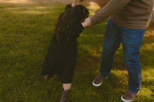 Adult and child holding hands while playing outdoors in warm sunlight.