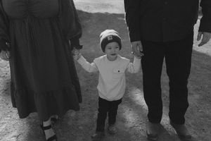 A black and white image of a small child holding hands with adults on a path.