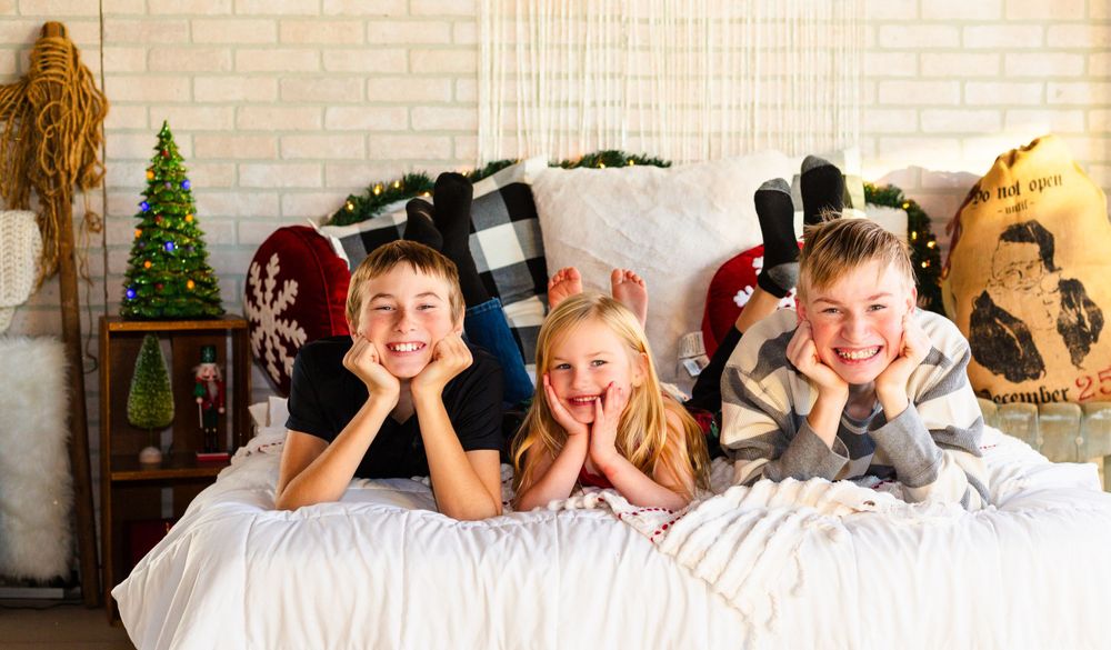 Three people posing playfully while lying on a bed with Christmas decorations in the background.