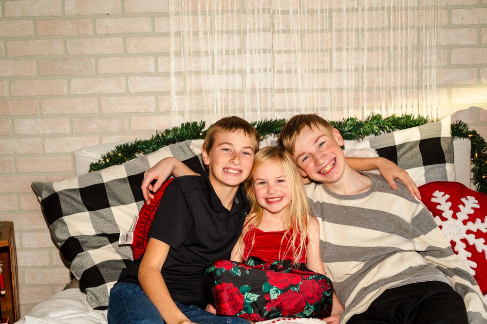 Three people posing together on a bed with buffalo check pillows and holiday decorations.