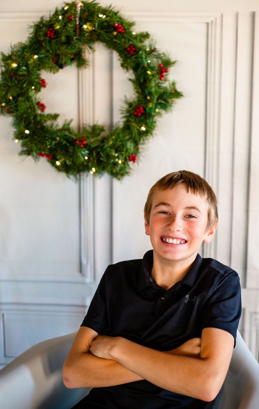 A holiday portrait with a lit Christmas wreath hanging on a white paneled wall.
