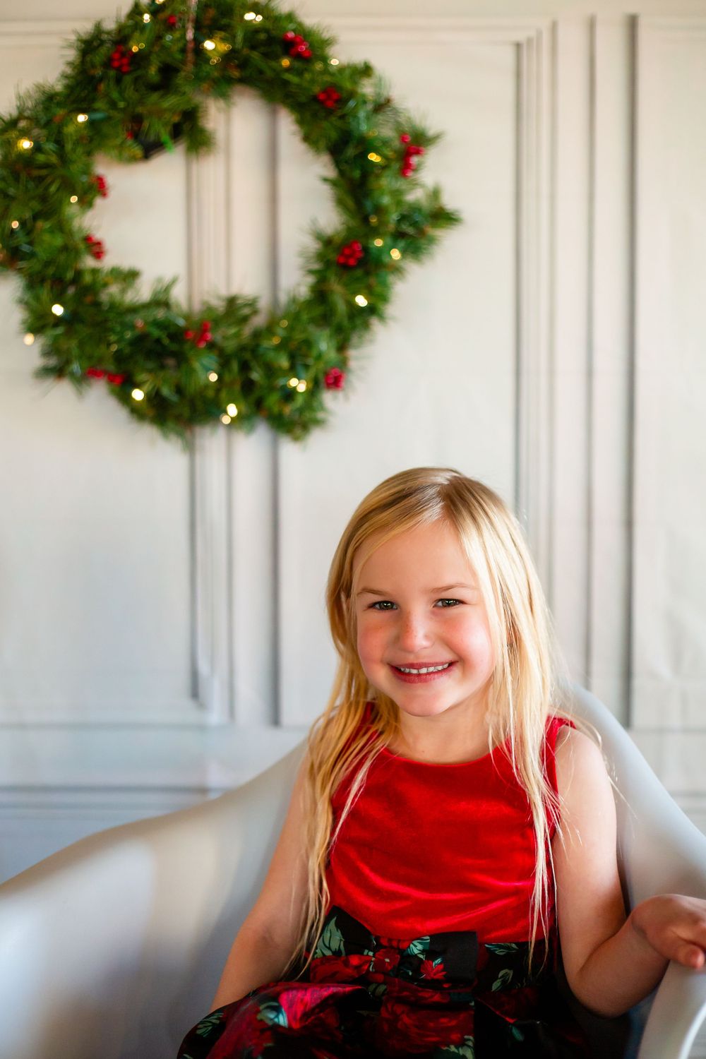 Portrait in front of a lit Christmas wreath on a white paneled wall.