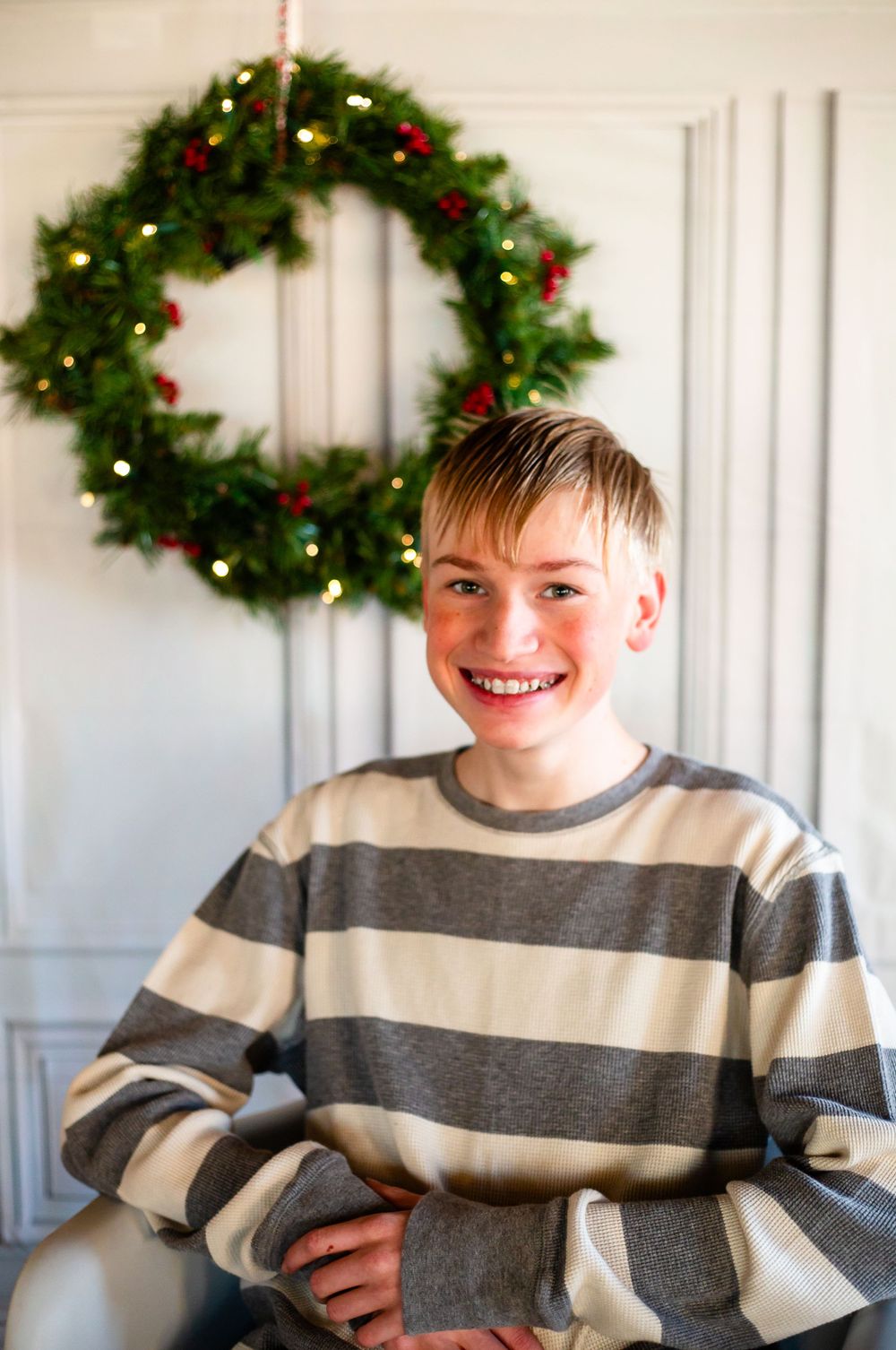 Portrait shot against a white wall with an illuminated Christmas wreath decoration.