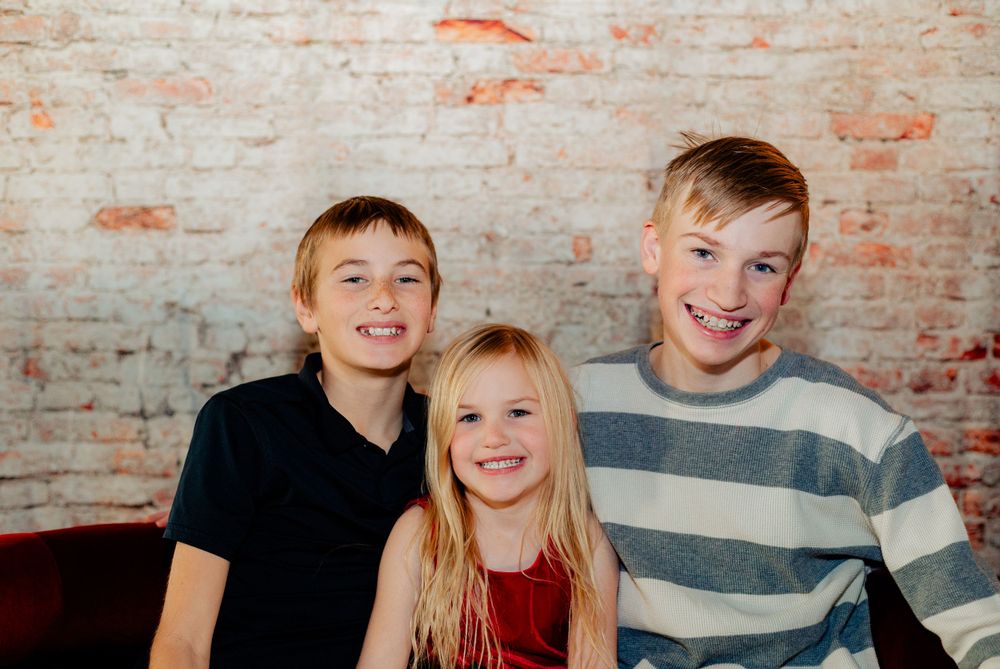 Three people smiling together against a rustic brick wall background.