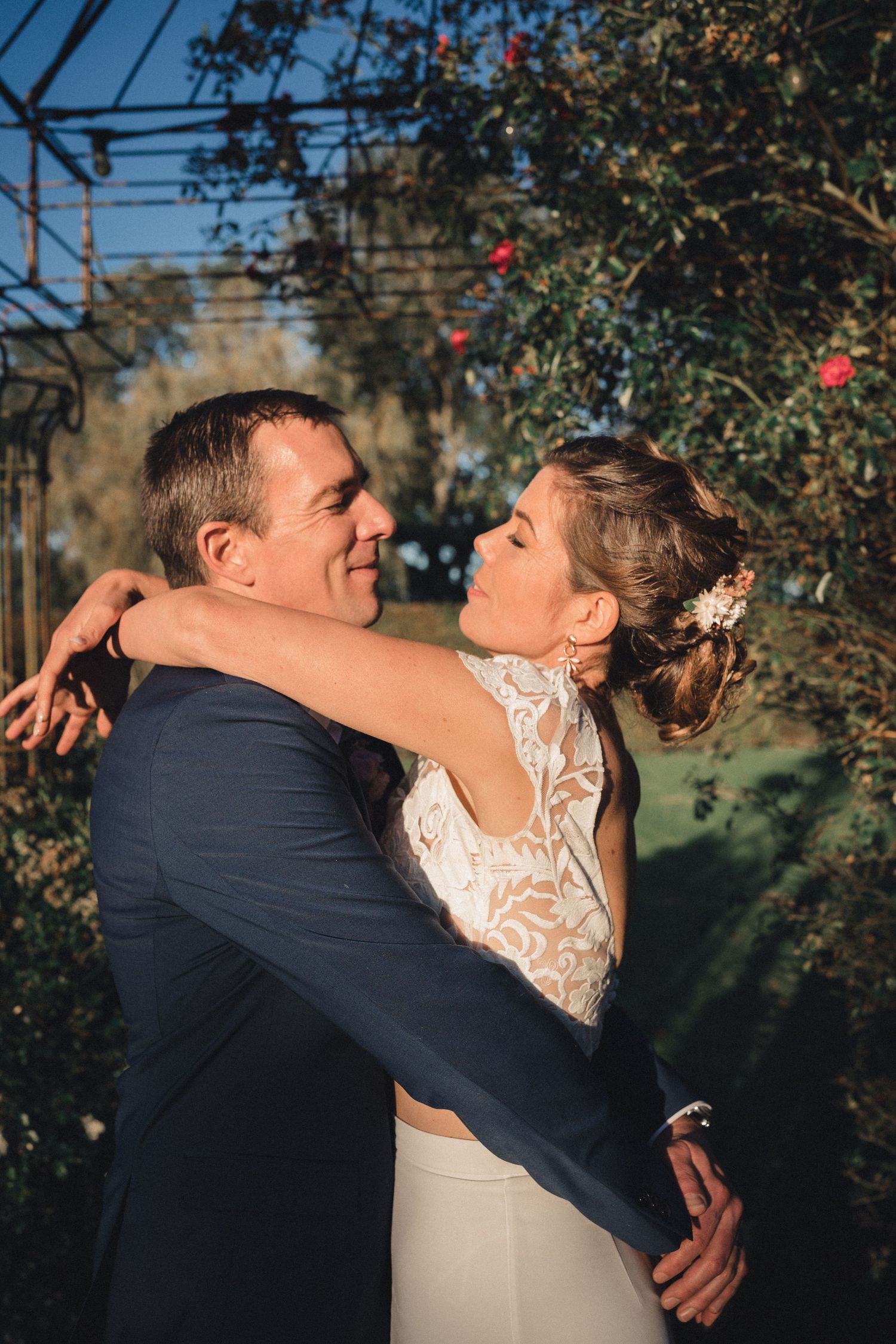 A romantic moment between newlyweds embracing outdoors with flowering trees in the background during golden hour.