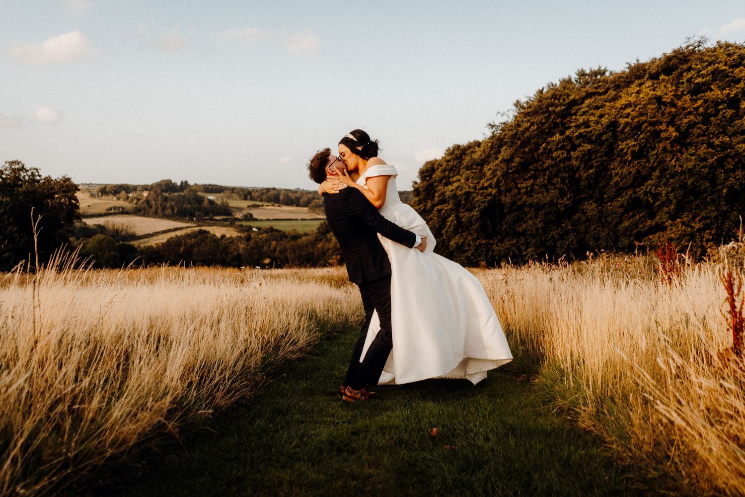 A romantic wedding couple shares an intimate moment in a grassy meadow at golden hour.