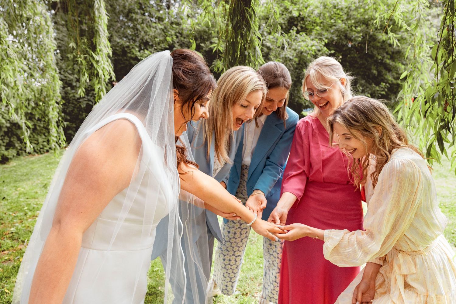 Wedding group gathers in a garden to admire rings and share a joyful moment together.