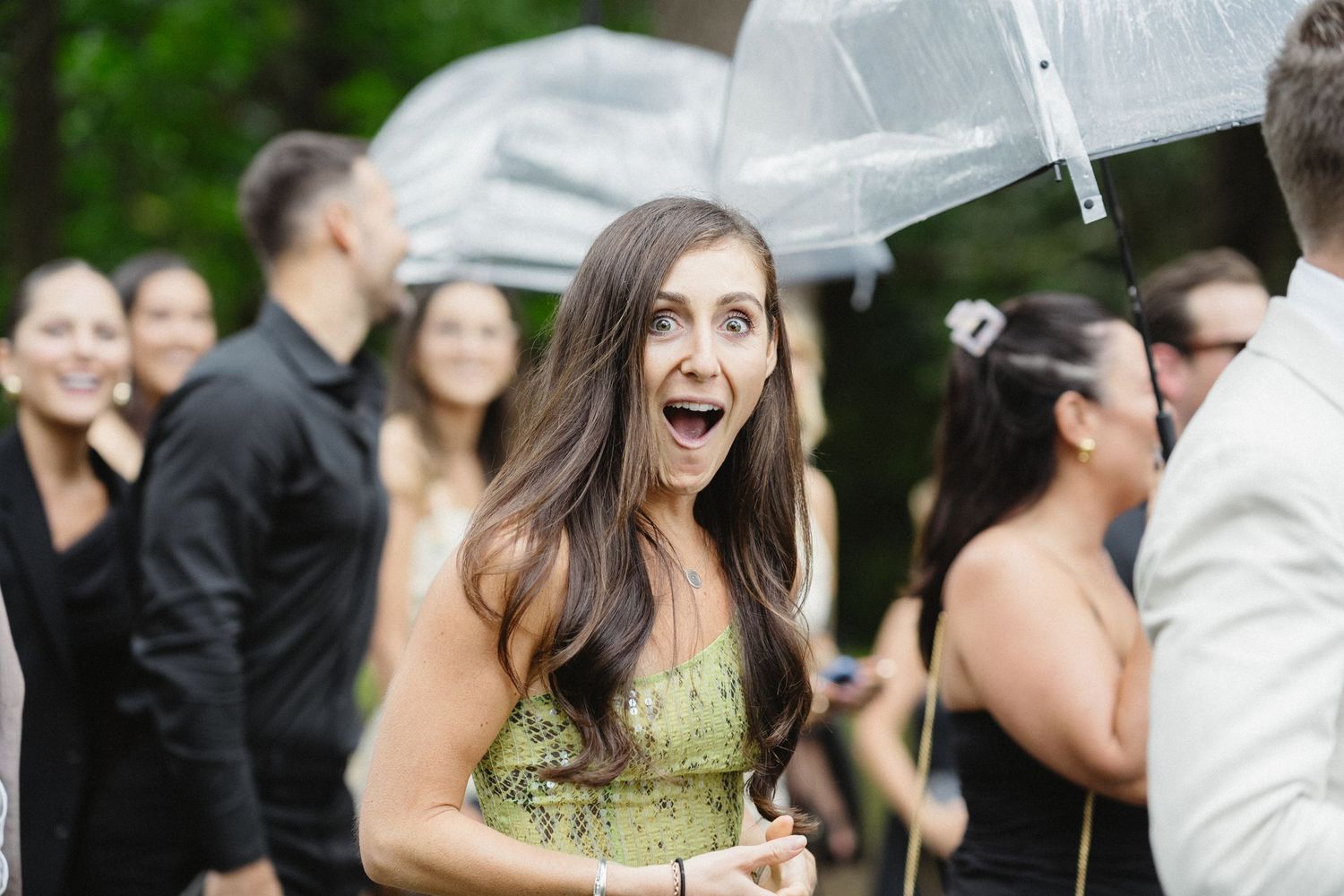 Guest reacts with excitement under clear umbrella at outdoor event.