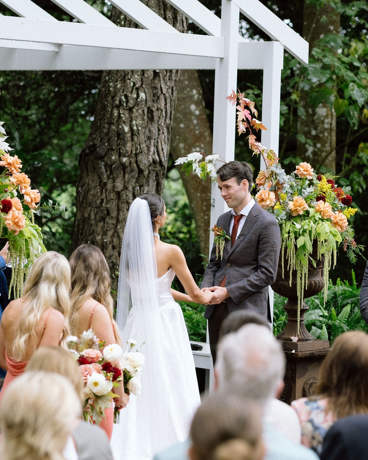 Outdoor wedding ceremony under white pergola with colorful floral arrangements.