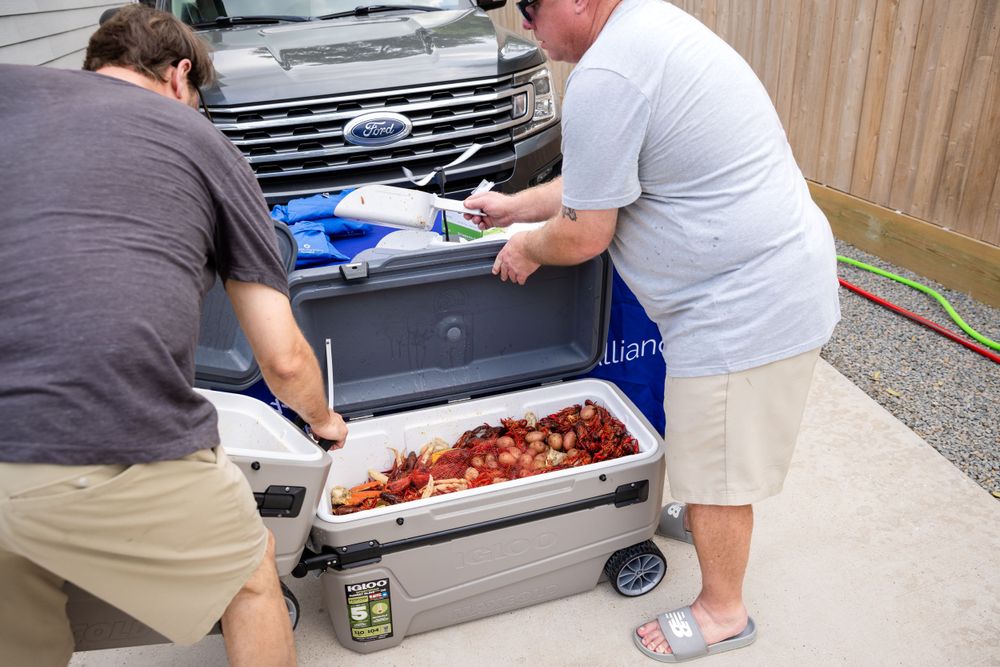 Two people loading coolers and supplies into the trunk of an SUV.