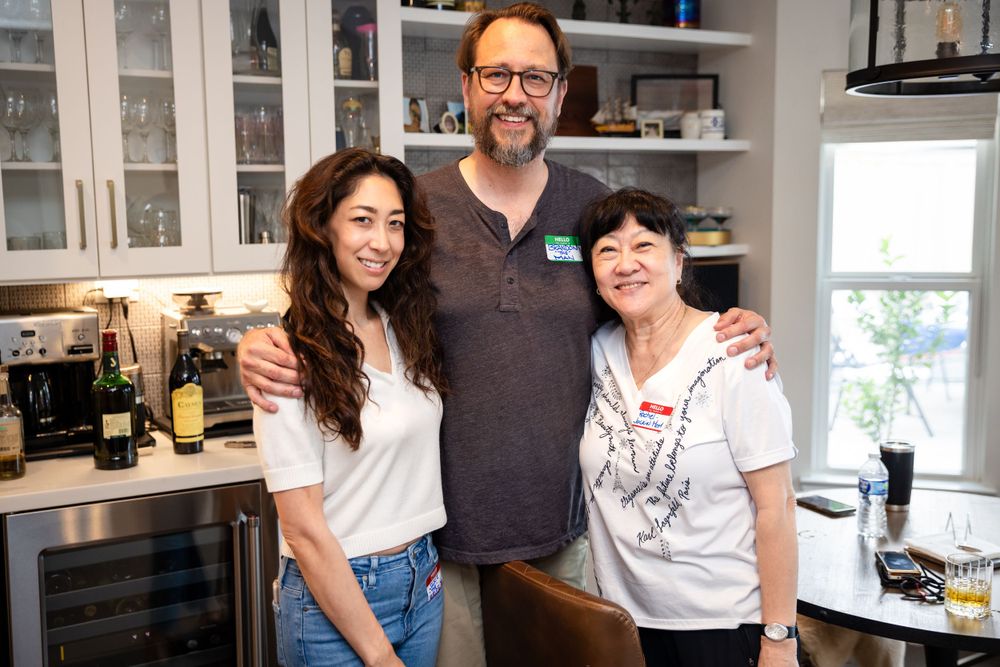 Three people pose together in bright modern kitchen with white cabinets.