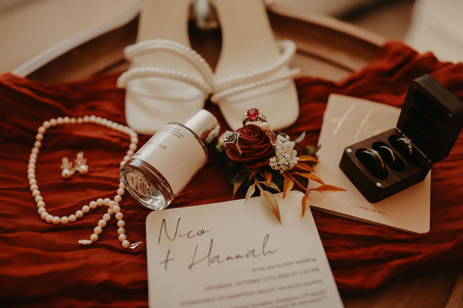 Wedding accessories including white shoes, pearls, rings and a note laid out on red velvet.