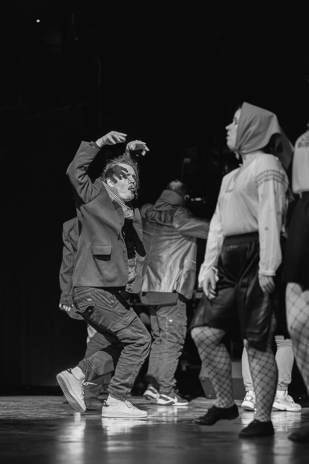 Dramatic black and white photo of dancers performing on stage, with one person in mid-movement wearing street style clothing.