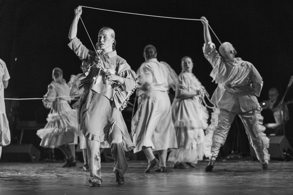 Vintage black and white photo of dancers performing a traditional folk dance with ropes on stage in flowing dresses and outfits.
