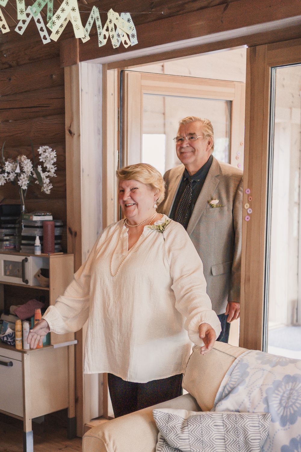 A couple in winter attire sharing a cheerful moment in a cozy cabin interior with light streaming through windows.