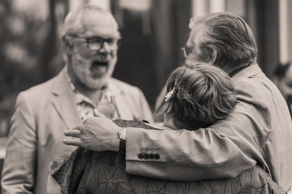 A black and white photo collage shows candid moments from a formal event with people laughing and embracing.