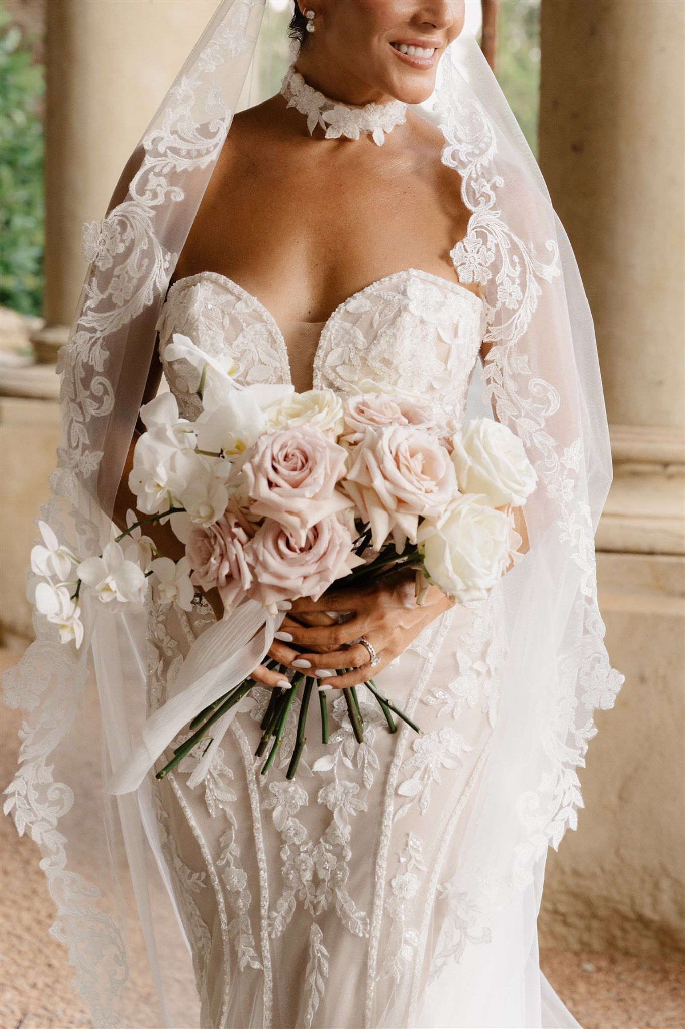 Close-up of bridal bouquet with blush roses and intricate lace wedding dress details.