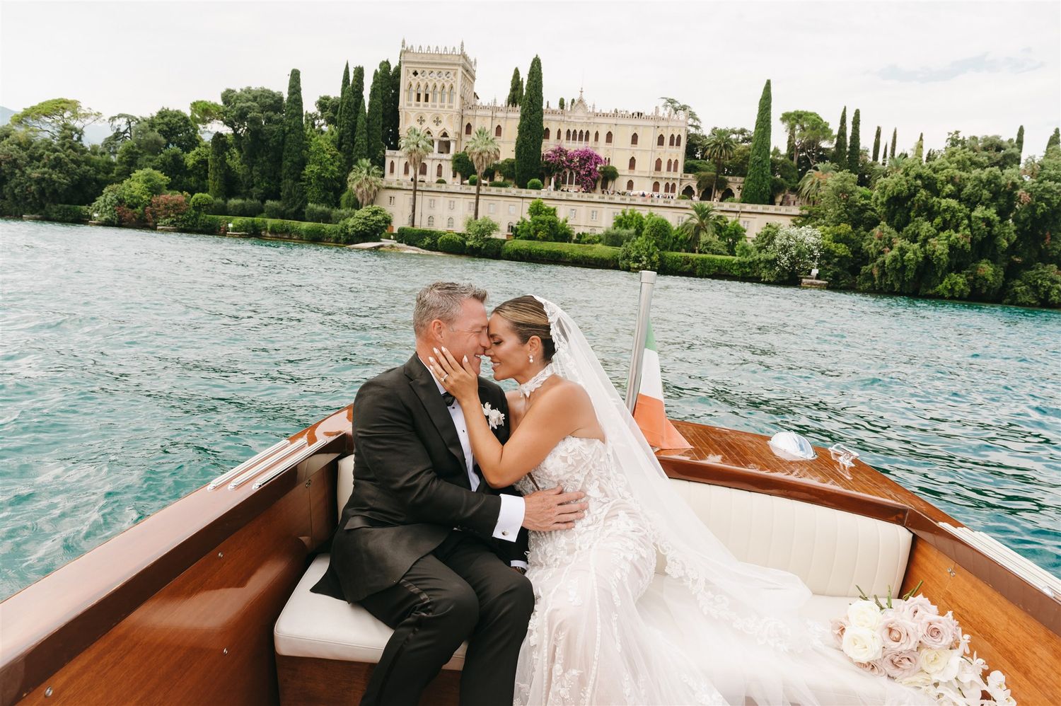 Wedding couple enjoying a romantic boat ride on a lake with historic buildings in the background.