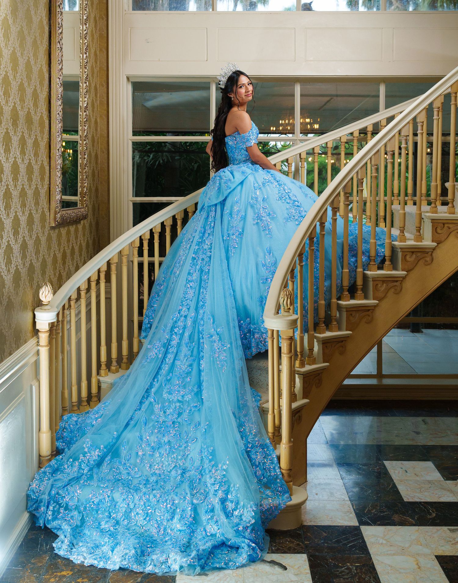Flowing blue ball gown with intricate lace details cascades down wooden staircase.