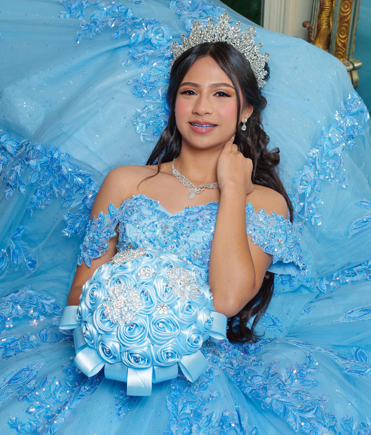A stunning light blue quinceañera dress with intricate floral details and crystal embellishments sparkles in natural light.