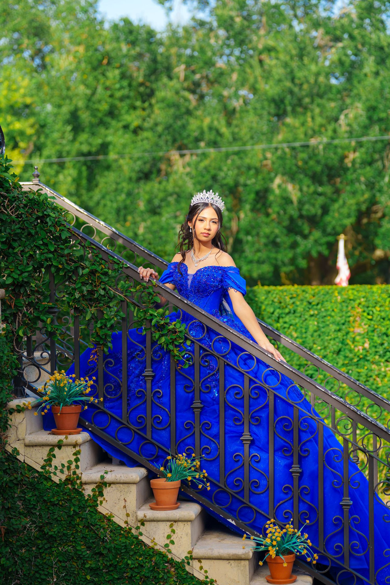 A regal blue ball gown contrasts beautifully against wrought iron railings and greenery on stone steps.