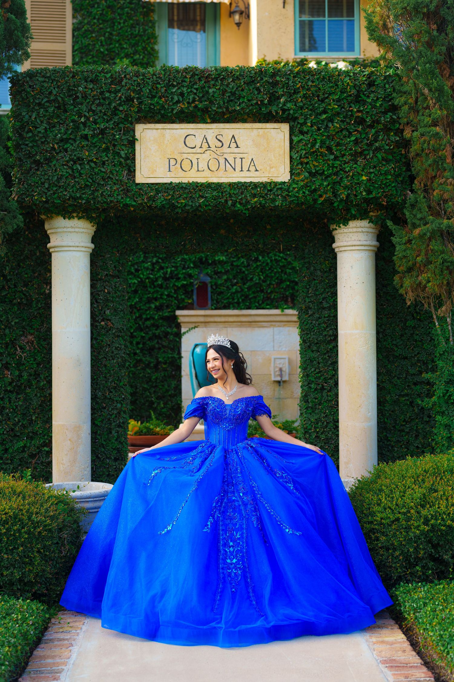 An elaborate royal blue ball gown displayed in front of Casa Polonia's classic columned entrance.
