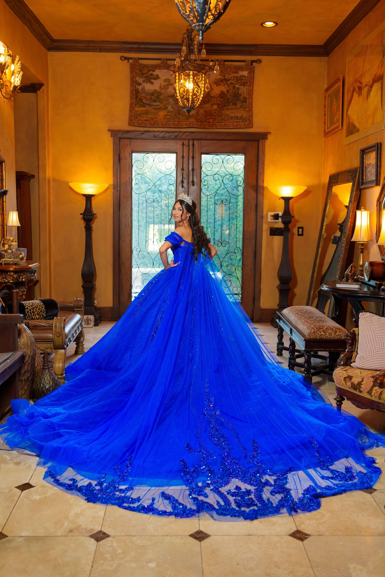 A stunning royal blue ball gown with an elaborate cathedral-length train displayed in an elegant room with warm lighting.
