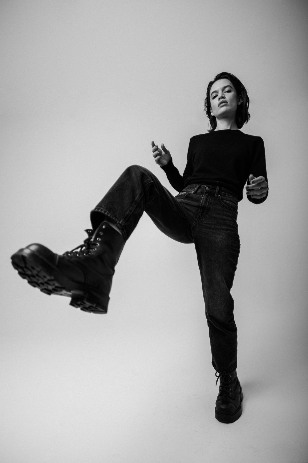 A dramatic black and white portrait of someone in a black outfit striking a rebellious pose with chunky combat boots.