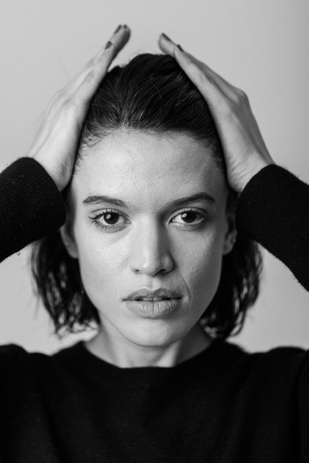 Dramatic black and white portrait showing someone with hands on head against a light background.